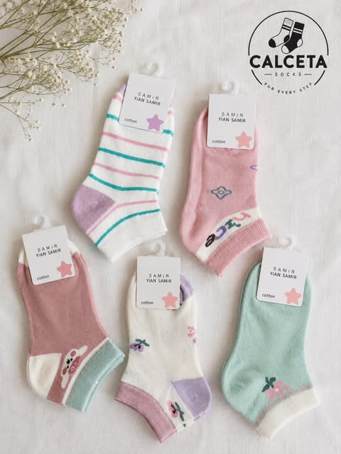 Cinq paires de chaussettes enfant pastel, menthe, rose ancien, lilas et blanc à rayures, disposées à plat sur du lin clair.